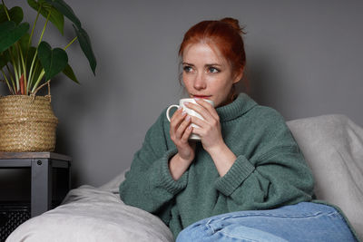 Portrait of young woman drinking water while sitting on bed at home