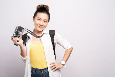 Portrait of young woman photographing while standing against white background