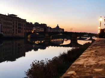 Bridge over river by buildings in city against sky during sunset