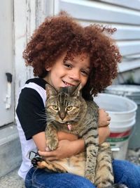 Portrait of smiling cute boy holding cat while sitting outdoors