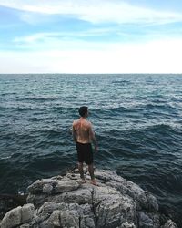 Rear view of man looking at sea from cliff against sky