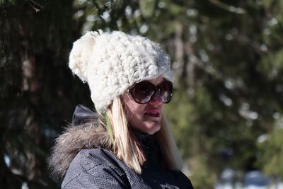 Woman wearing sunglasses and knit hat while looking away in forest during winter