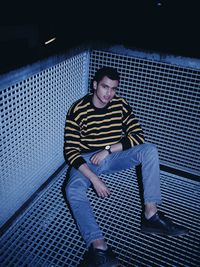 High angle portrait of young man sitting on metal at night