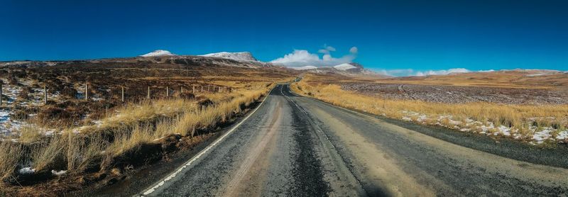Panoramic view of road leading towards mountains against blue sky