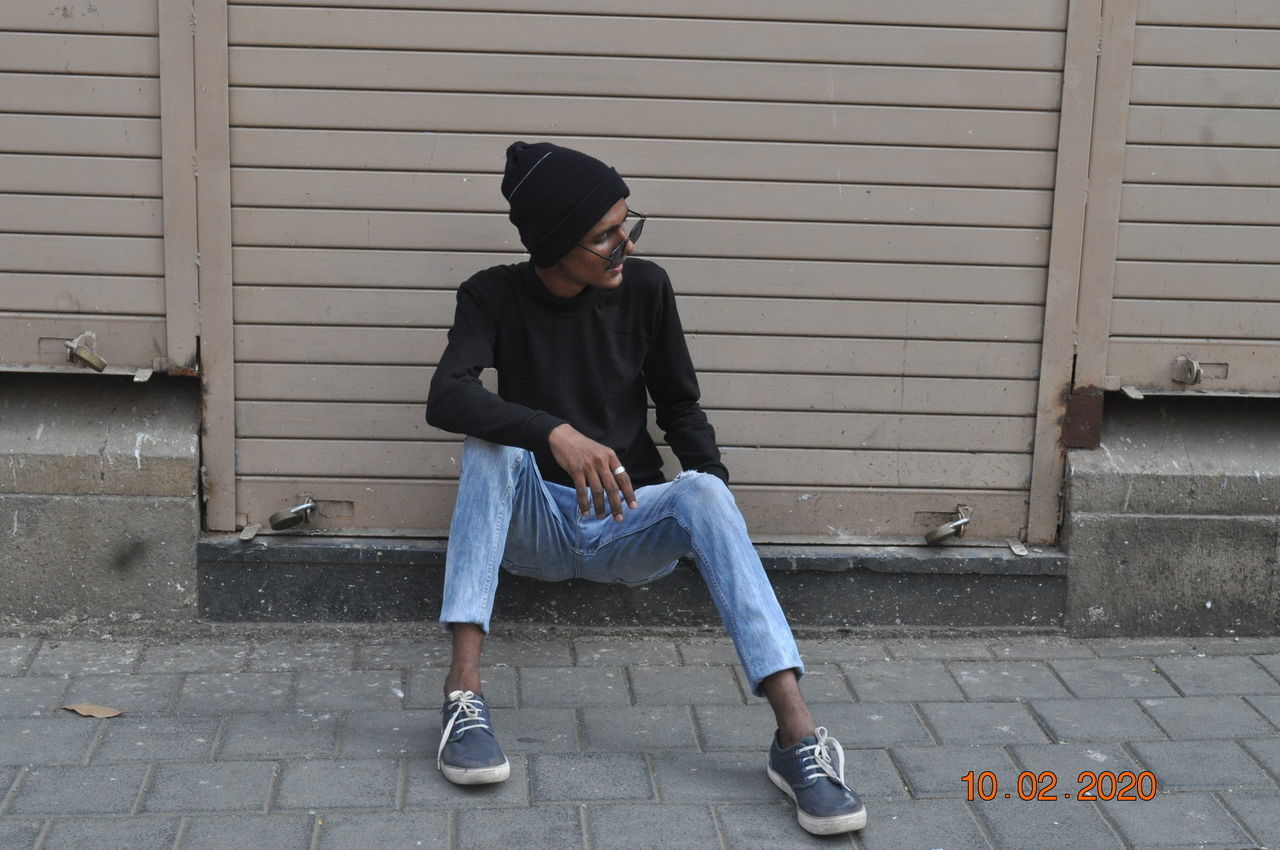 FULL LENGTH OF YOUNG MAN SITTING AGAINST WALL