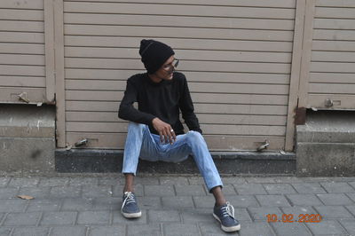 Full length of young man sitting on footpath