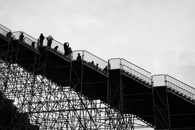 Low angle view of people walking staircase against sky
