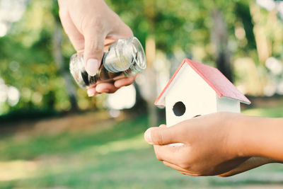 Cropped image of hands holding model house and coins in jar