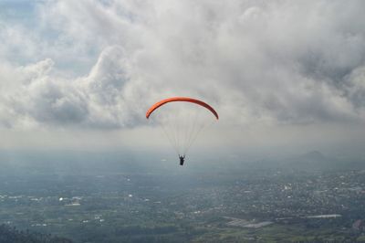 Person paragliding over cityscape against sky