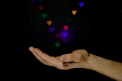 Close-up of hand against illuminated light over black background