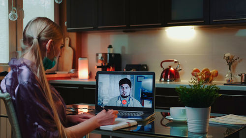 Woman using phone while sitting on table at home