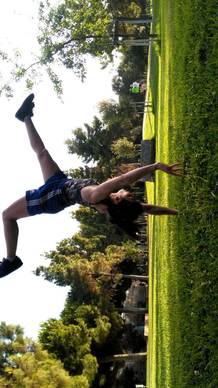 YOUNG WOMAN IN MID-AIR AGAINST TREES