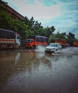 Cars on wet road against sky during rainy season