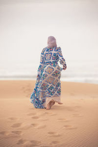 Rear view of woman walking on sand at beach