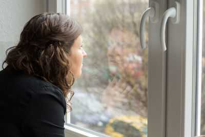 Close-up of woman peering out of window