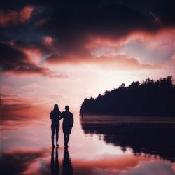 Silhouette men standing on lake against sky during sunset