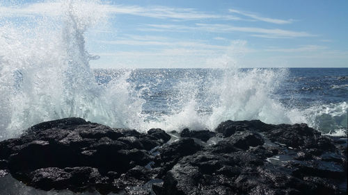 Waves splashing on rocks against sky