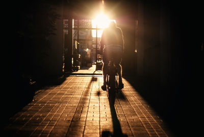 Rear view of man cycling in alley at sunrise