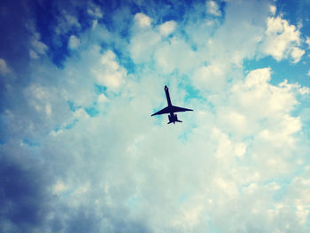 Low angle view of airplane flying against cloudy sky