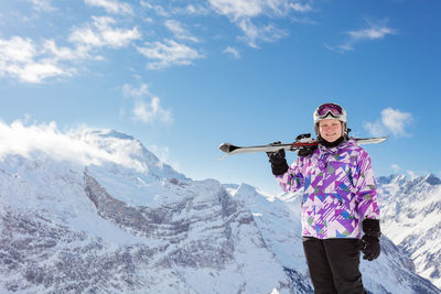 Young woman standing on snowcapped mountain against sky