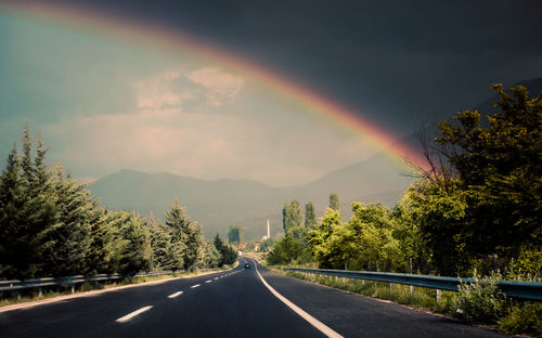 Rainbow over road against sky