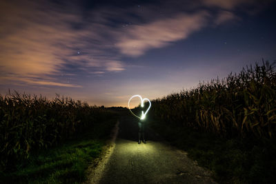 Person with heart shape light painting standing on road against sky
