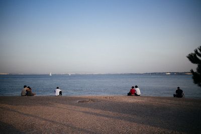 People sitting on beach against clear blue sky