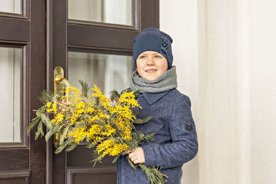 Portrait of a boy in a blue coat with a bouquet of mimosa in his hands in the park. spring, 