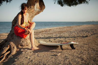 Woman sitting on beach by sea against sky