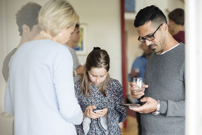 Man and girl using phone while having drink at home in social gathering