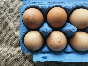 Directly above view of brown eggs in blue carton on jute