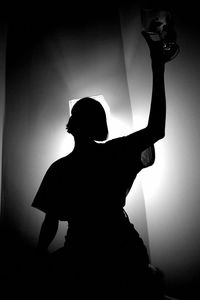 Silhouette woman with arms raised standing against wall