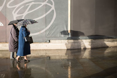 People with umbrella walking on wet footpath by building