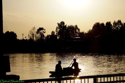 Silhouette people sitting on lake in front of trees