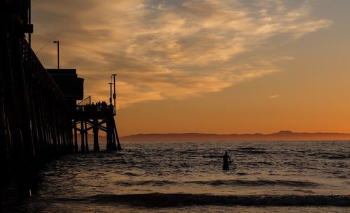 Silhouette pier over sea against orange sky