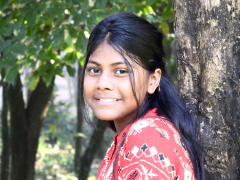 Portrait of young woman standing against tree