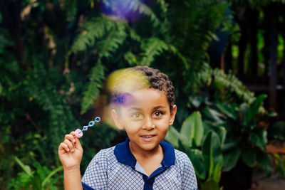 Portrait of smiling boy holding plant against plants