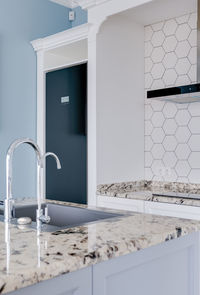 White modern kitchen with marble countertops, white diamond-shaped tiles and a modern black fridge