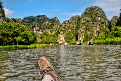 Low section of man on riverbank against sky