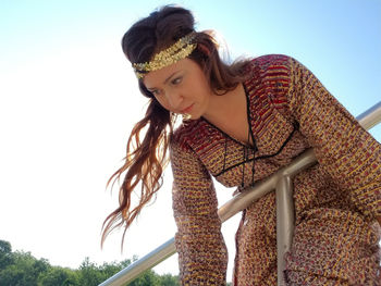 Low angle view of young woman hanging on railing against sky