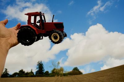 Low angle view of hand holding machinery on field against sky