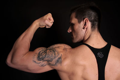 Rear view of athlete flexing muscle against black background