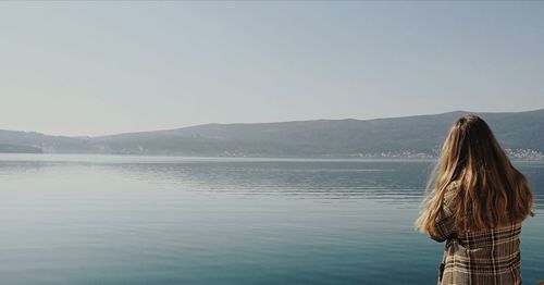 Rear view of woman looking at lake against clear sky