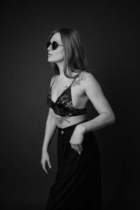 Portrait of young woman standing against black background