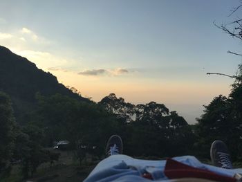 Low section of man relaxing on landscape against sky