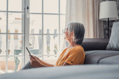 Side view of young woman using digital tablet while sitting at home