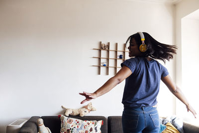 Carefree woman wearing headphones while dancing at home