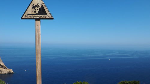 Information sign by sea against blue sky