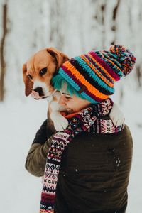 Rear view of young woman carrying beagle while standing in forest during winter