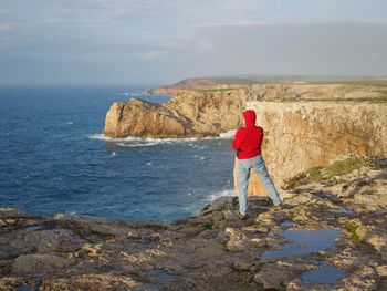 Rear view of man standing on rock by sea against sky